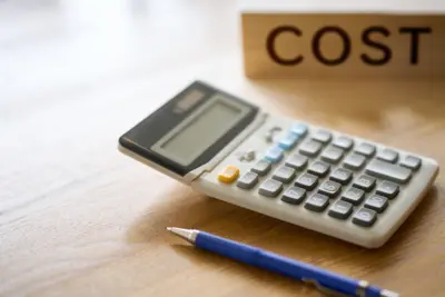 Calculator and pen on a wooden desk next to a block spelling COST, illustrating forehead reduction surgery costs in Turkey