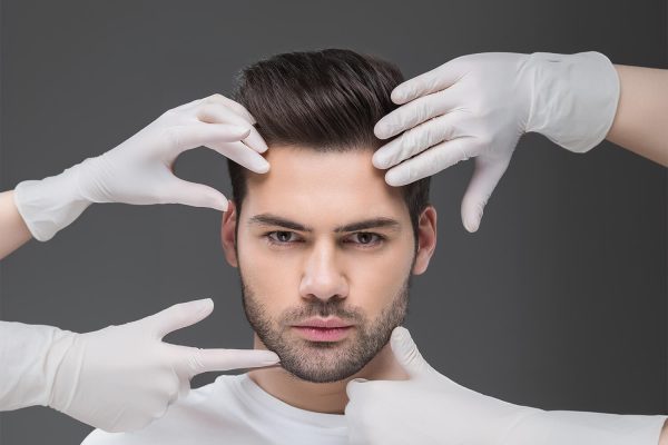 handsome man and doctors hands, isolated on grey, skin care concept